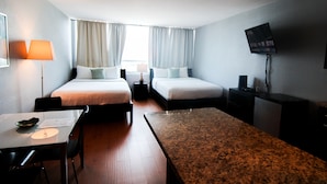 A hotel room with two beds, a desk, a television, and a dining area.