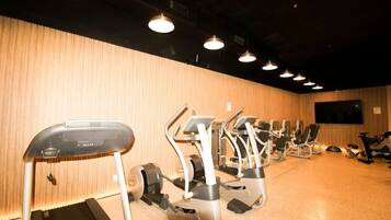 A gym with various cardio machines, a television screen on the wall, and a wooden wall.