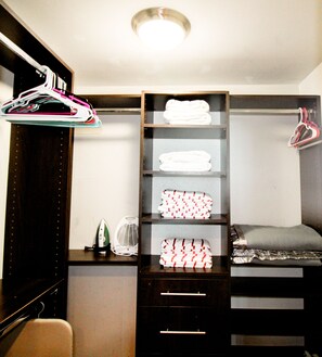 A bedroom with a bunk bed, a wardrobe with hanging clothes, and a shelf with folded towels.