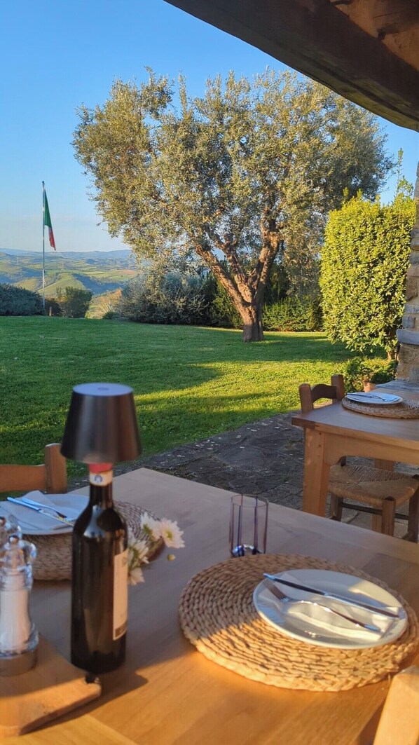 A table set outdoors with a bottle, glasses, and a flag in the background. - Podere Prataccio (Scansano)