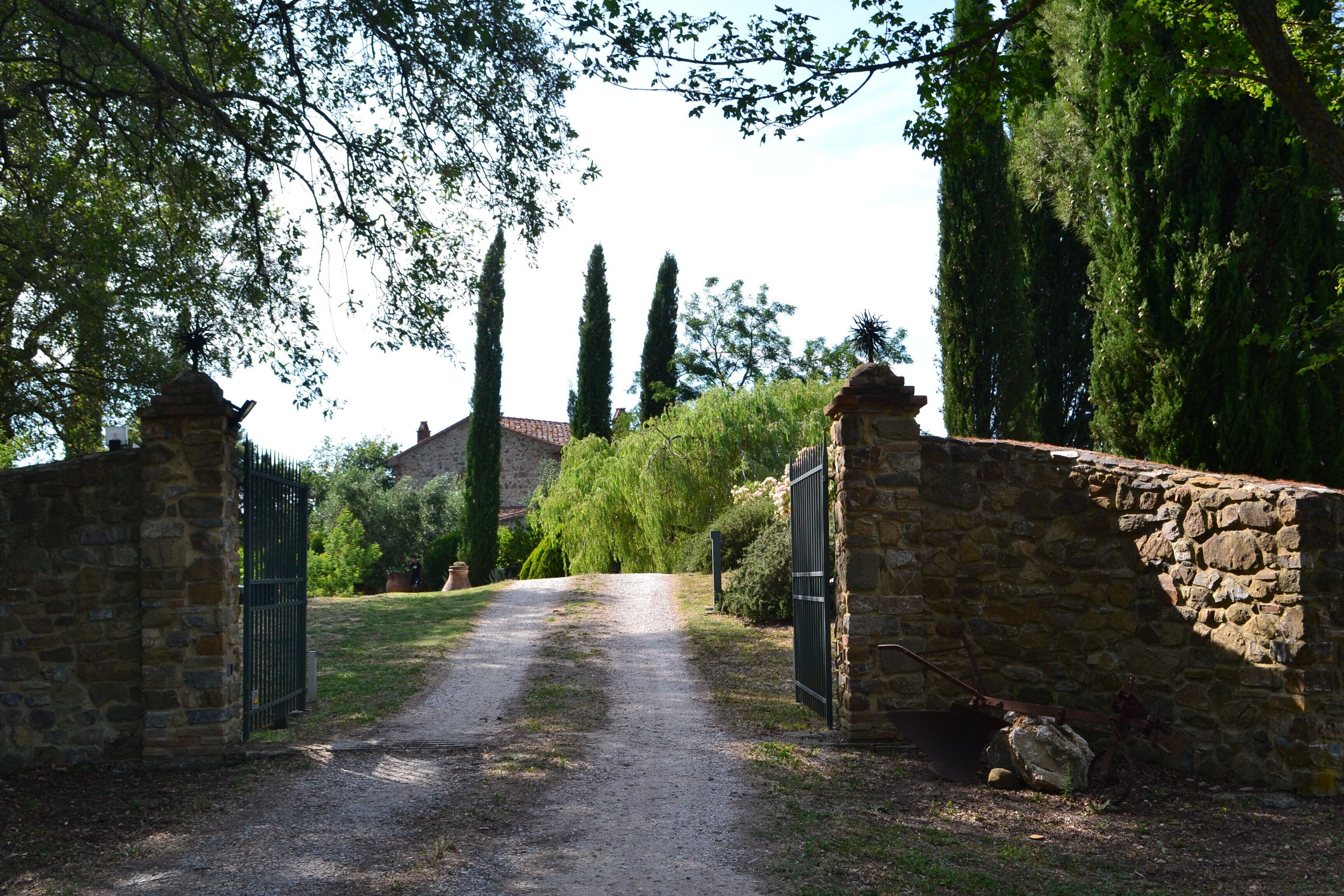 A stone gate leading to a path, surrounded by trees and a stone wall.