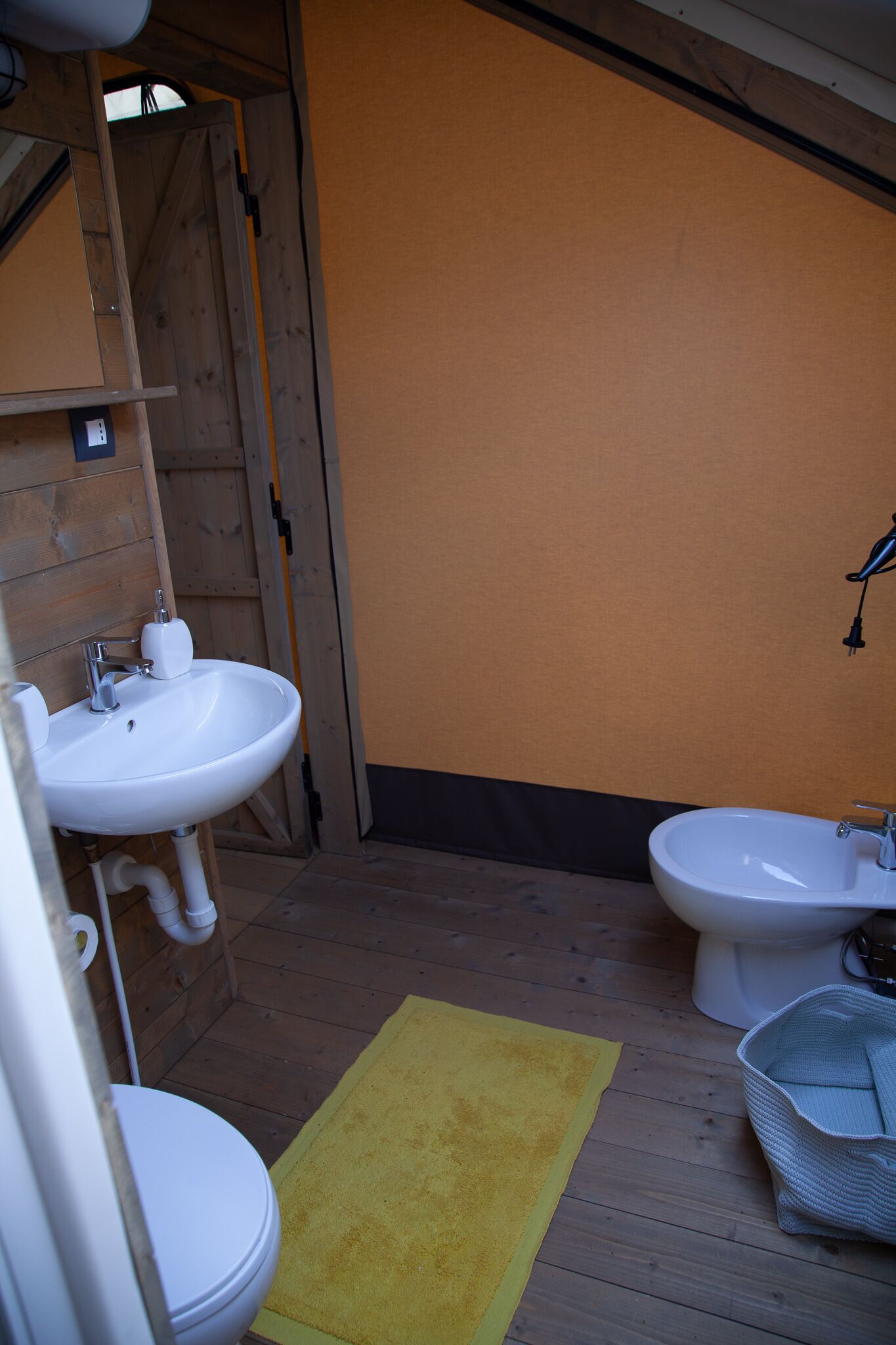 Een badkamer met houten wanden, een geel vloerkleed, een witte wastafel en een toilet.