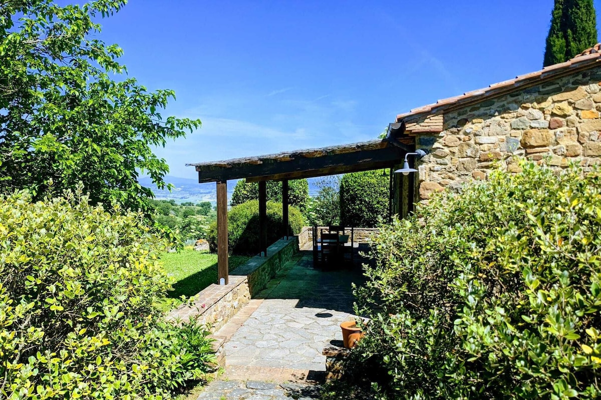 A stone pathway leading to a rustic stone building with a wooden pergola.