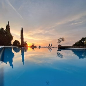 A clear swimming pool with reflections, a sunset, and a few people walking. - Podere Prataccio (Scansano)