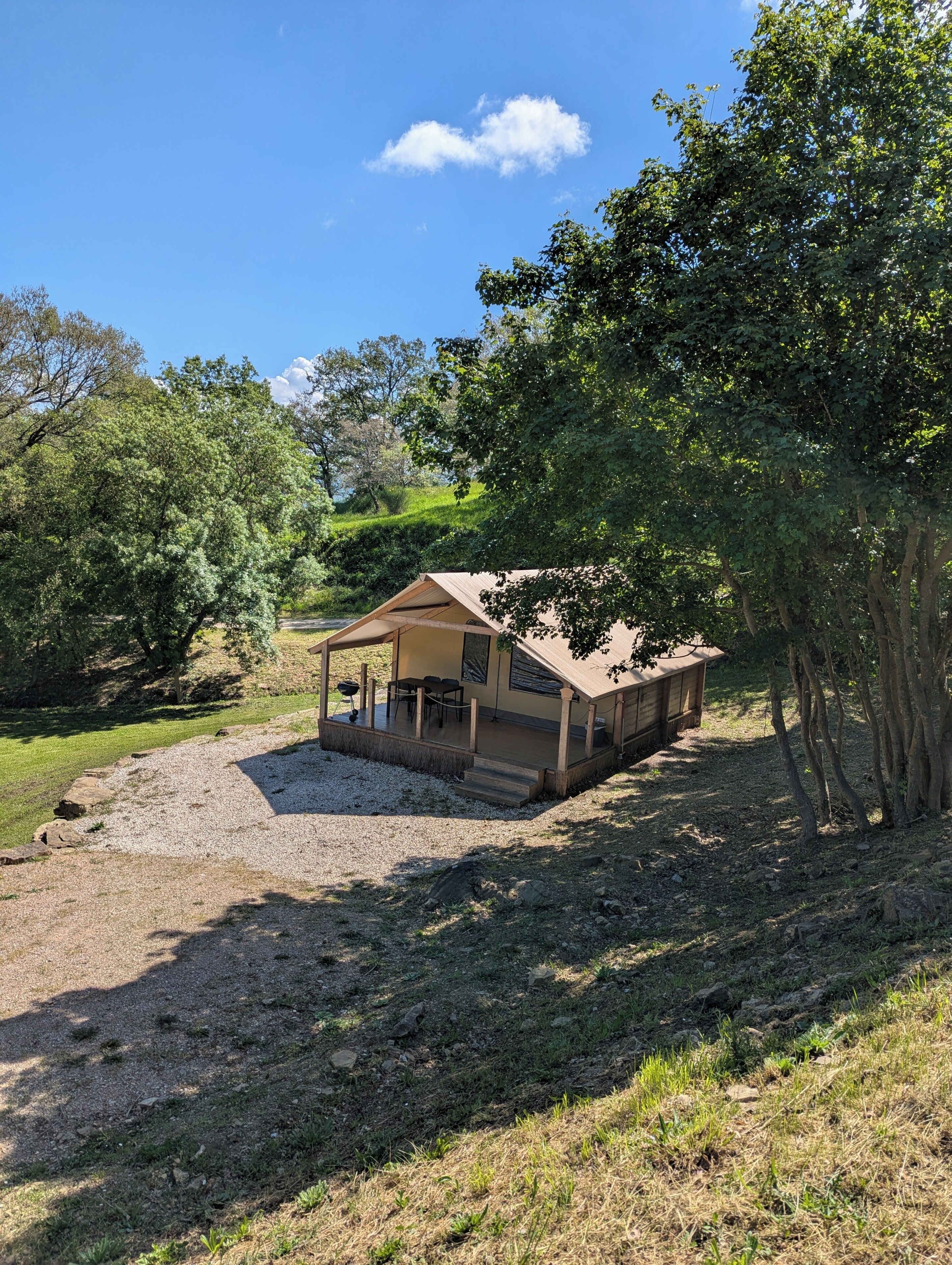 Een klein, laag gebouw met een veranda en zitplaats buiten, omringd door bomen en een grindpad.