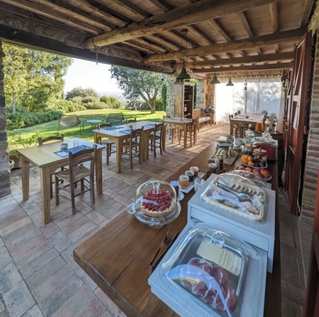 An outdoor dining area with stone tables and chairs, a buffet with various food items, and a view of a garden and trees.