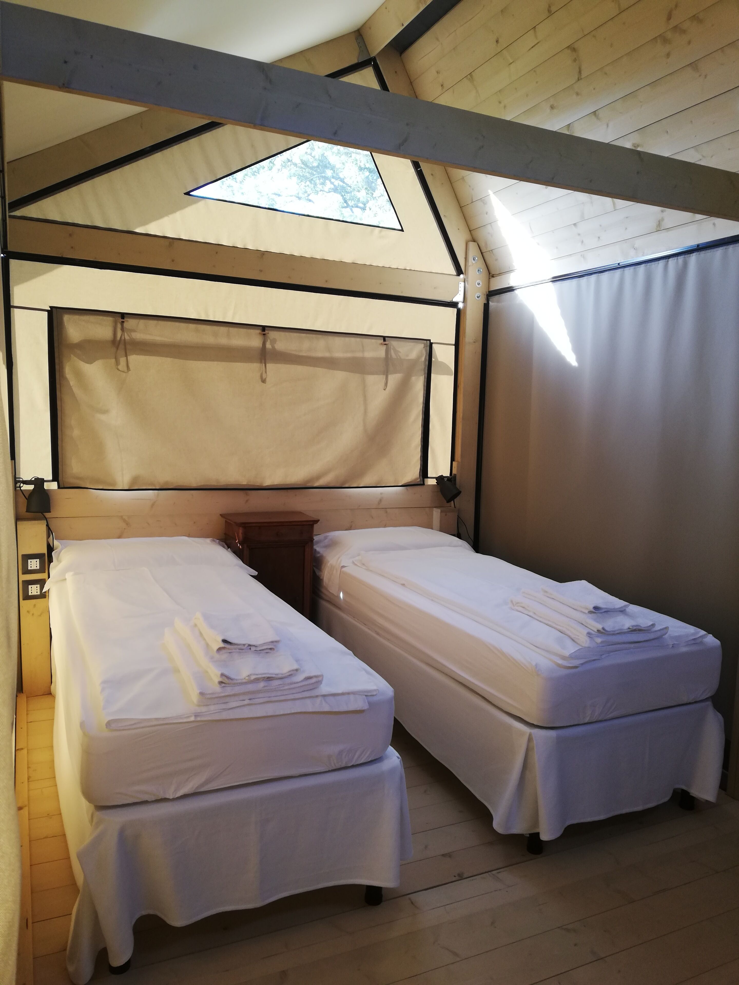 Une pièce aménagée comme une tente, avec deux lits, un plancher en bois et une lucarne.