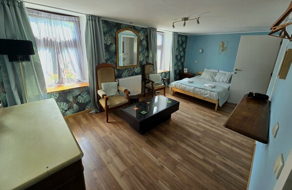 Ein Zimmer mit einem Bett, einem Sessel, einem Tisch und einem Spiegel.