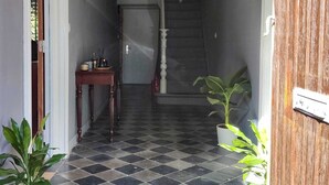 Un couloir avec un sol à carreaux, une porte en bois, une petite table avec une plante et un paillasson.