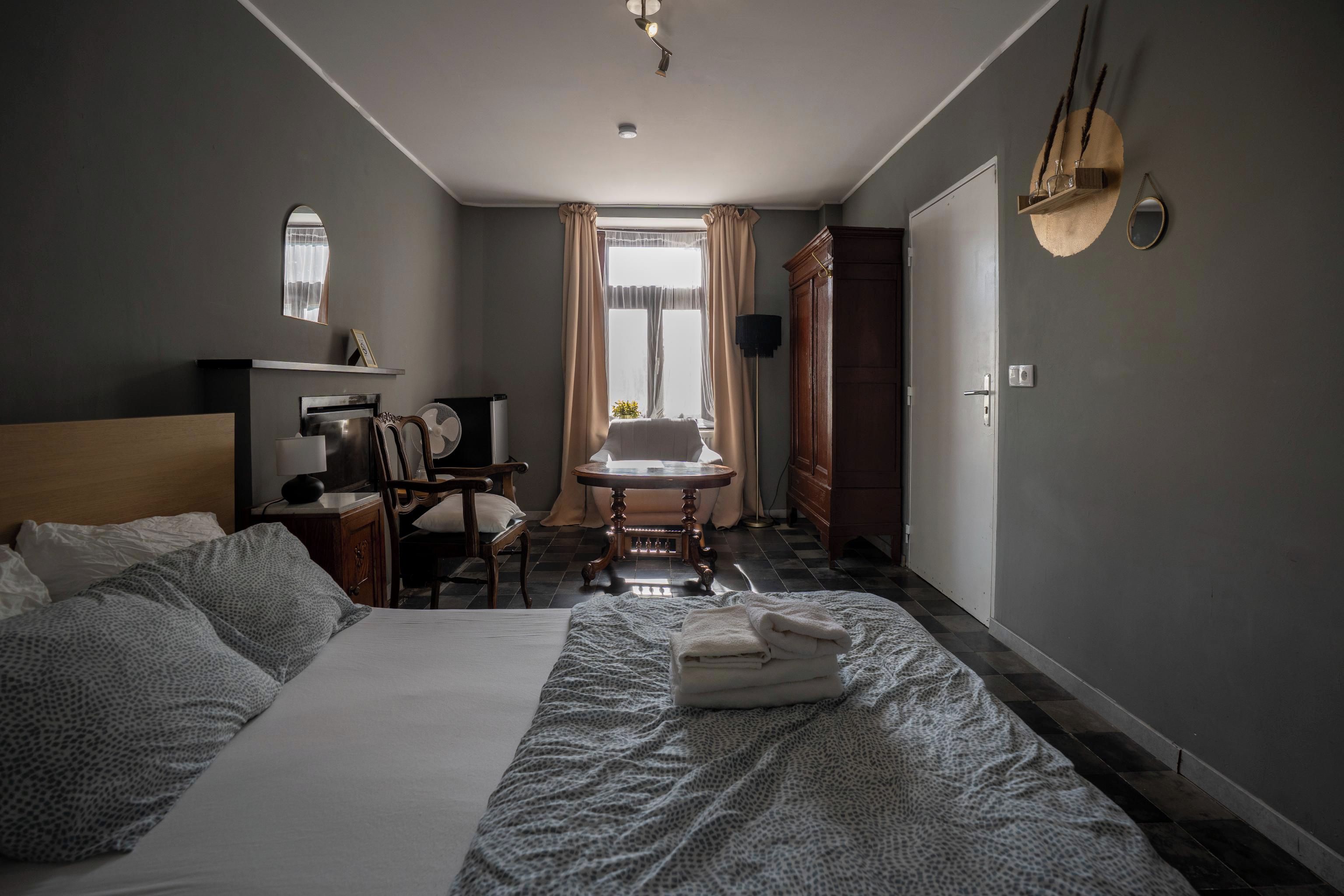 A hotel room with a bed, a desk, a chair, a table, and a wardrobe.