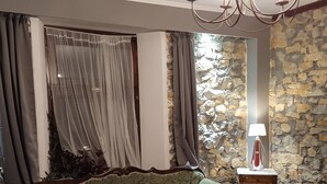 Une pièce avec un canapé à motifs verts, une table basse ronde en marbre, un lustre et un mur en pierre.