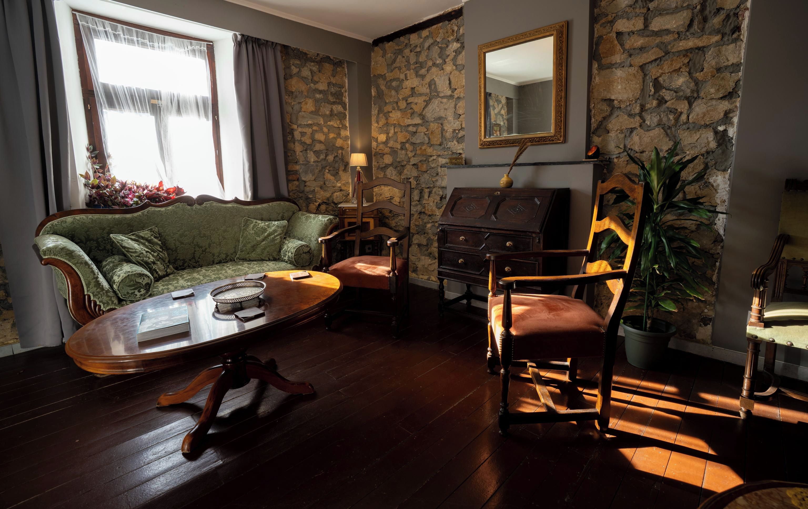 Une pièce avec un mur en pierre, un canapé vert, une chaise en bois, une petite table et un miroir.