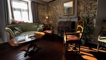 Une pièce avec un mur en pierre, un canapé vert, une chaise en bois, une petite table et un miroir.