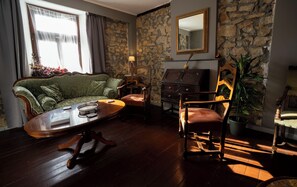 A room with a stone wall, a green sofa, a wooden chair, a small table, and a mirror.