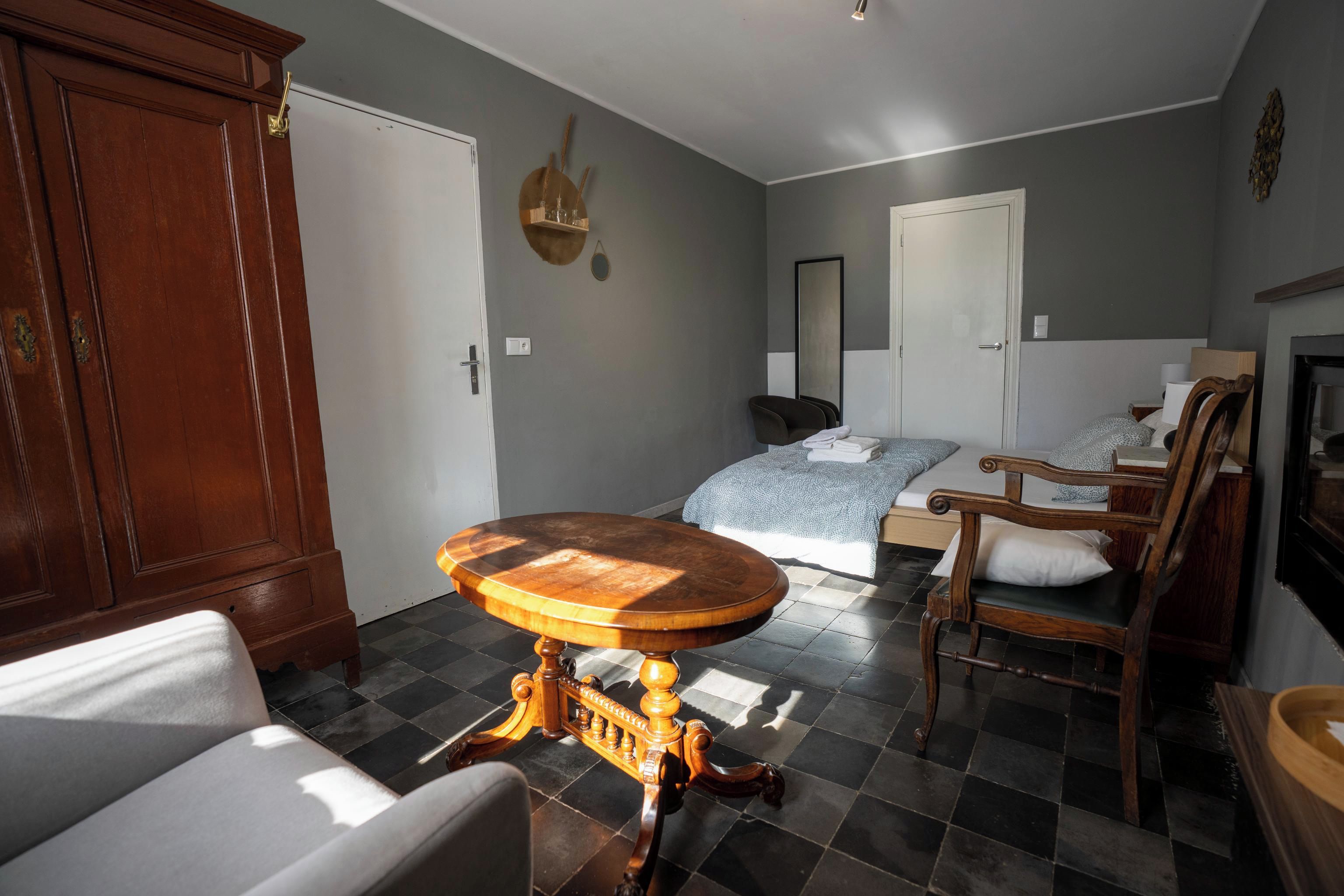 A room with a bed, a round wooden table, a chair, and a wardrobe.