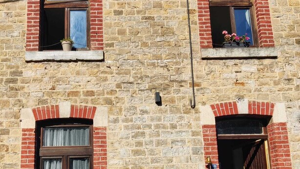 Un immeuble à plusieurs étages, avec des murs en briques et de nombreuses fenêtres, dont certaines sont dotées de volets.