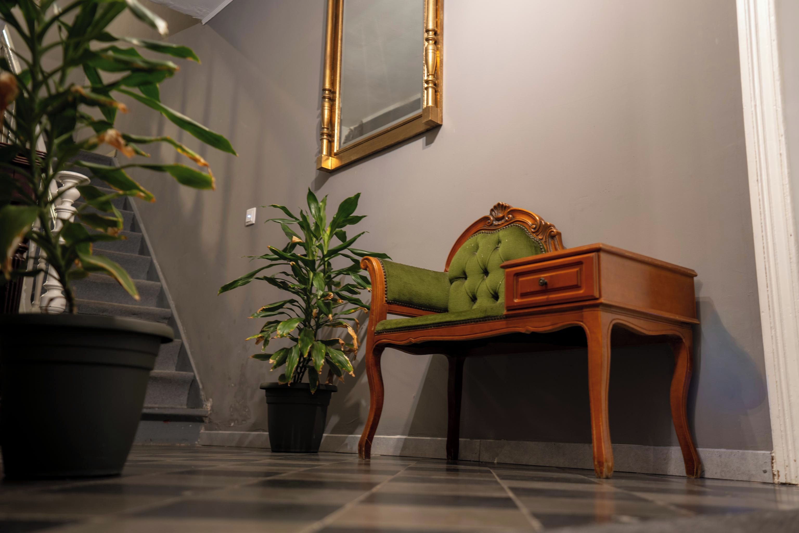 Une pièce avec un bureau en bois, une chaise rembourrée de tissu vert, une plante en pot et un escalier.