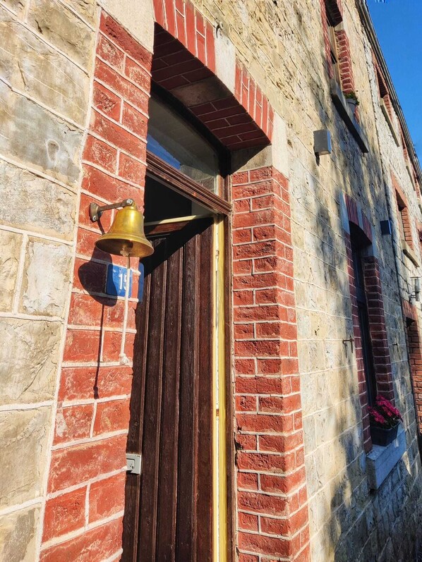 A brick building with a wooden door and a bell mounted on the wall.