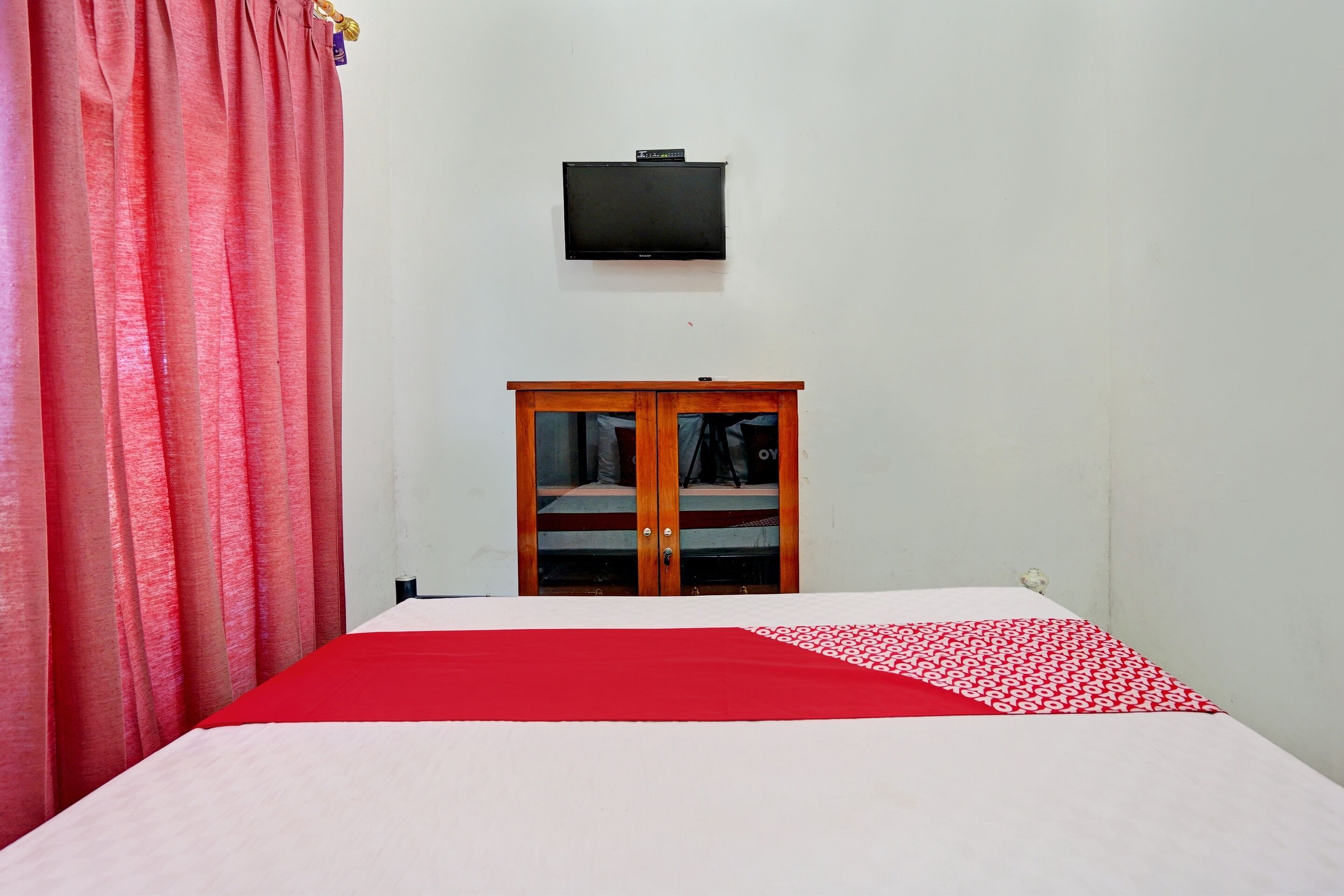 Una habitación con una cama, un televisor montado en la pared y un armario de madera.