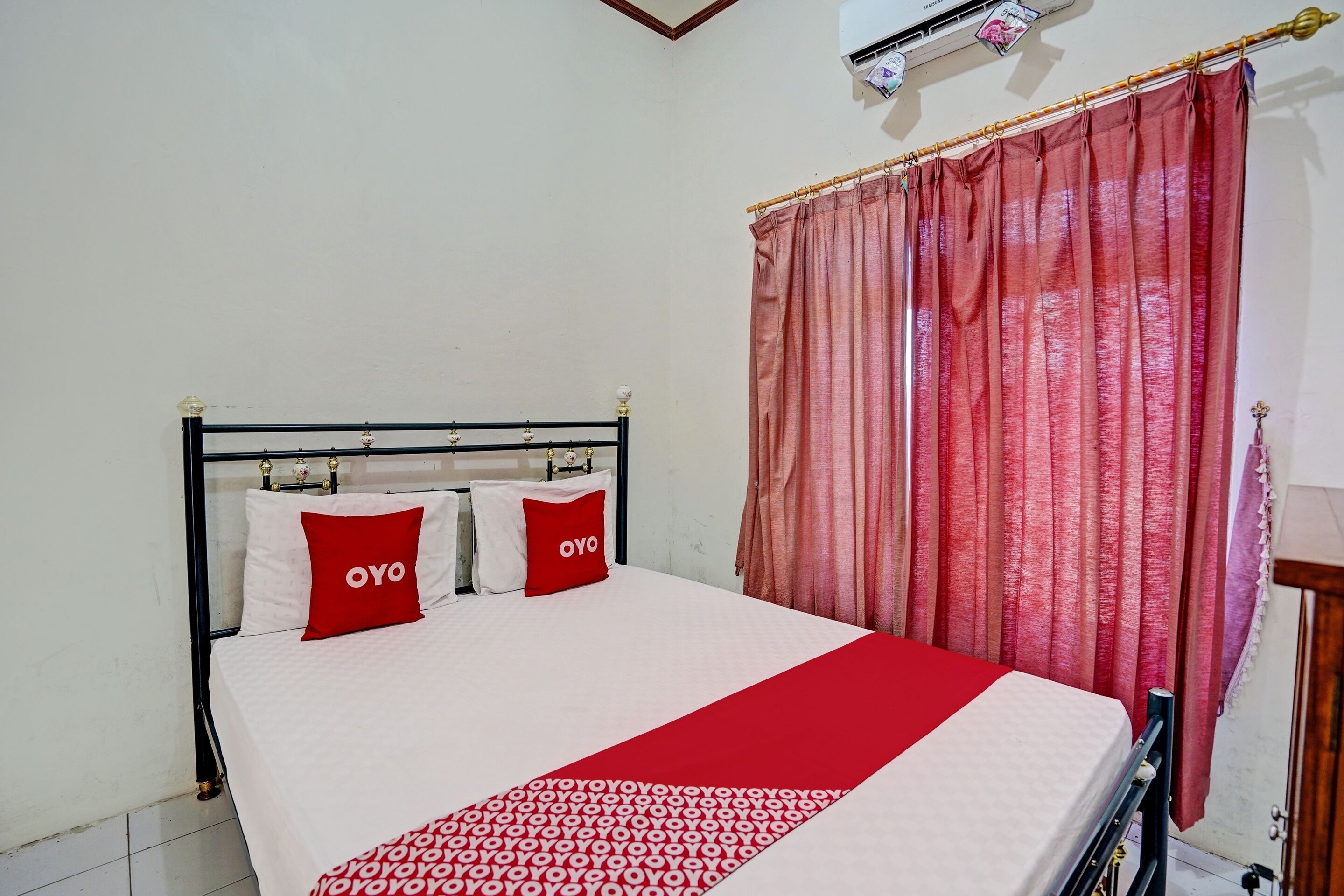 Una cama bien tendida con una colcha roja y blanca y dos almohadas rojas con la palabra 'OYO' escrita en ellas.