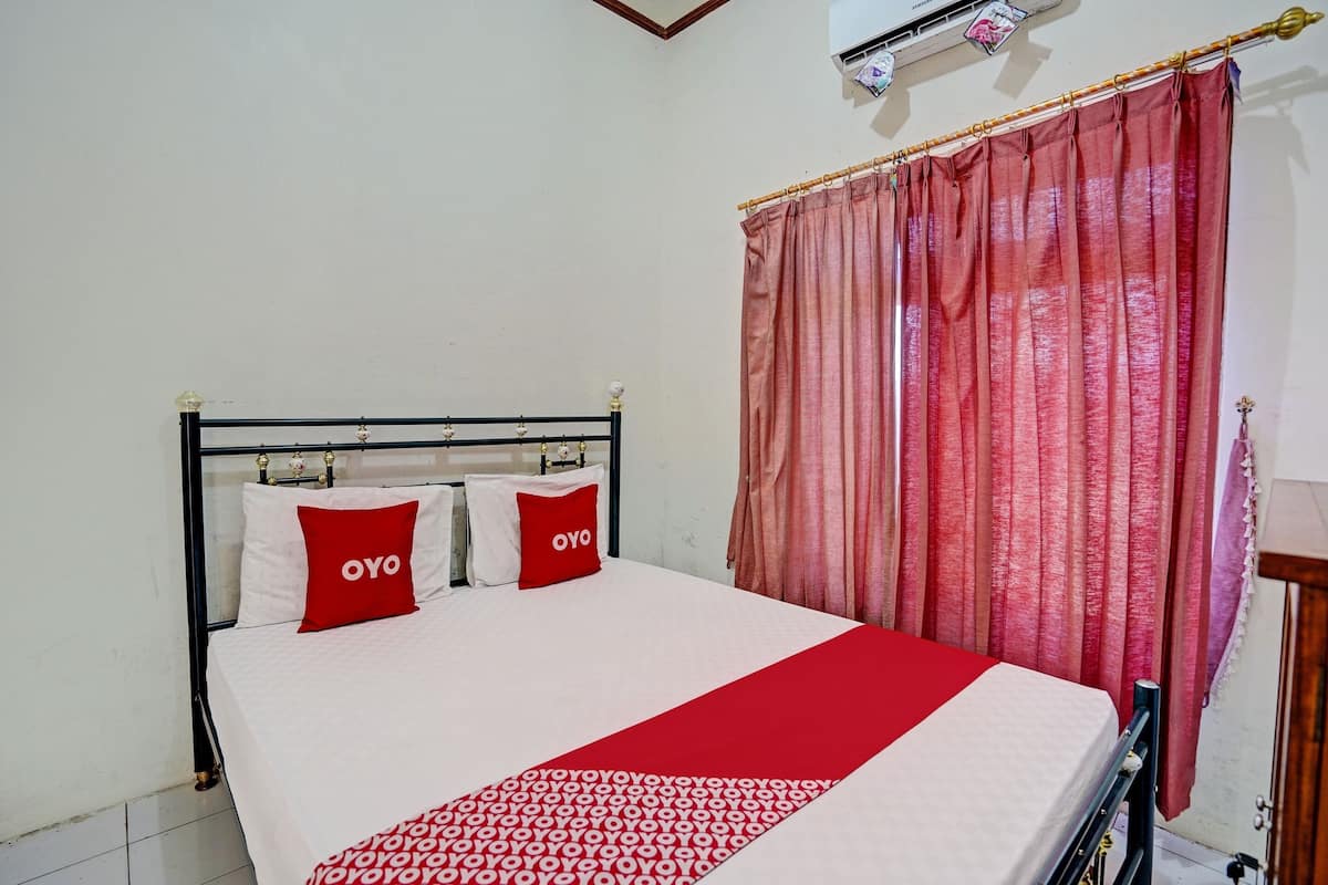 Una cama bien tendida con una colcha roja y blanca y dos almohadas rojas con la palabra 'OYO' escrita en ellas.