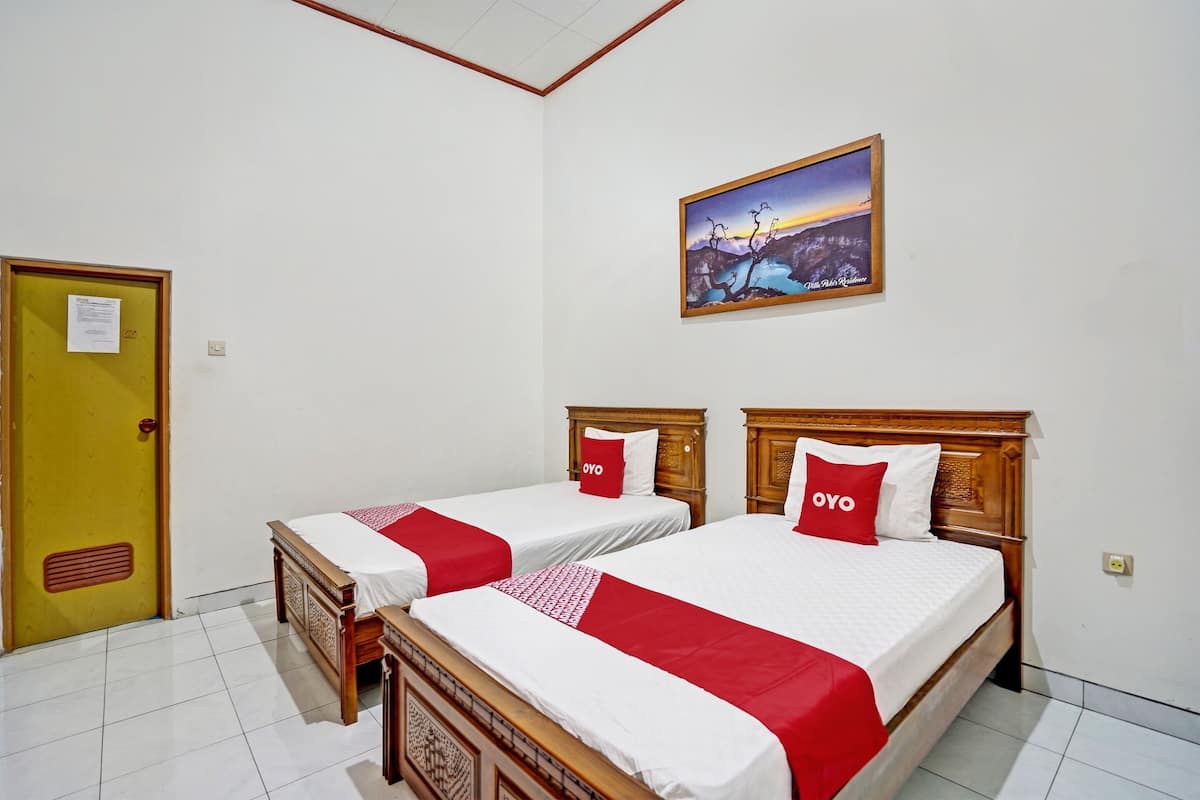Habitación de hotel con dos camas de madera, cada una con una colcha roja y blanca y almohadas a juego.