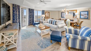 A spacious living room with a sofa, armchair, coffee table, and a dining area with a table and chairs.