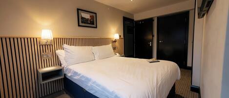 A hotel room with a large bed, two bedside tables with lamps, a wall-mounted picture, and a wardrobe.