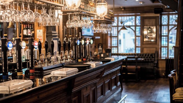 A bar area with a long counter, multiple taps, and hanging glasses. - Lower Turks Head  (Manchester)