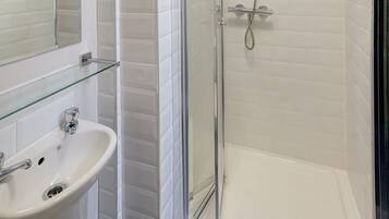 A bathroom with a glass shower enclosure, a white sink, and a mirror above the sink.