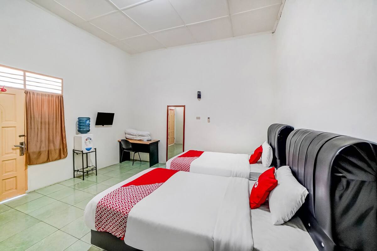 Une chambre d’hôtel avec deux lits, un bureau, une chaise, une télévision et une porte.