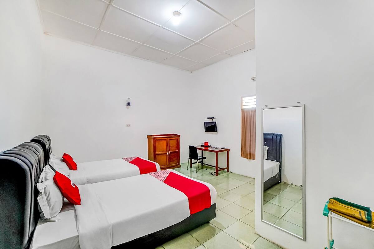Une chambre d’hôtel avec deux lits, un bureau, une armoire, une télévision et un miroir.