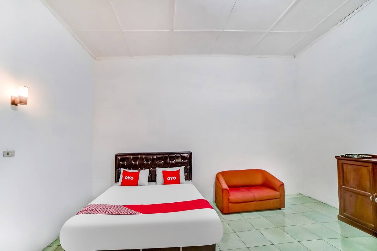 Une pièce comprenant un lit, une couvre-lit rouge et blanche, une chaise rouge et une armoire en bois.