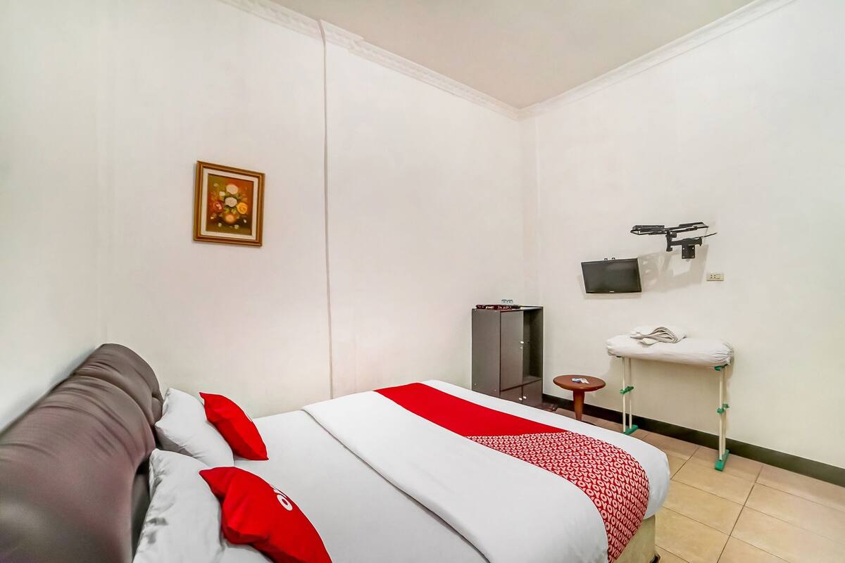 Une chambre d’hôtel avec un lit, une couvre-lit rouge et blanche, un canapé gris, une petite table, un téléviseur fixé au mur et un meuble.