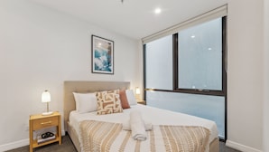 A hotel room with a large bed, a nightstand with a lamp, a framed picture on the wall, and a window with a view.