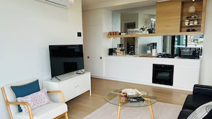 A modern living room with a flat-screen TV, a glass coffee table, and a sofa with cushions.