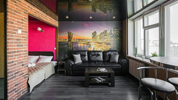 A modern room with a brick wall, a black leather sofa, a coffee table, and a cityscape mural on the wall. - Elegant Apartment in Minsk (Minsk)