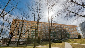 A multi-story building with a brick facade, surrounded by a grassy area with trees and a paved walkway. - Elegant Apartment in Minsk (Minsk)