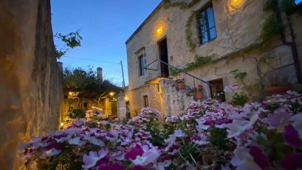 Un bâtiment en pierre doté d’un escalier et d’un jardin où poussent des fleurs roses et blanches.