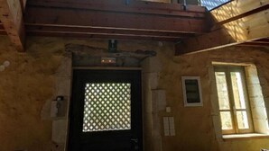 Une pièce aux hauts plafonds, dotée d’un balcon en bois, d’une grande fenêtre ornée d’un motif en treillis et d’une porte présentant un motif similaire.
