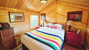 A cozy wooden cabin bedroom with a large bed, wooden dresser, and two bedside tables with lamps.
