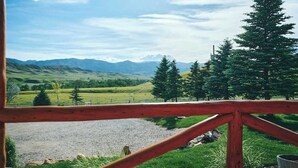 A view from a wooden balcony overlooking a valley with mountains, a river, and trees.