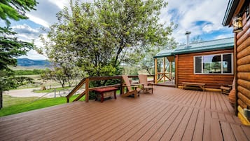 A wooden deck with outdoor furniture, a large tree, and a cabin with a metal roof.