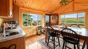 Un intérieur en bois comprenant une cuisine, un coin repas et de grandes fenêtres donnant sur l’extérieur.