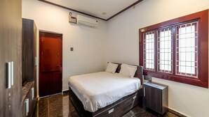 Ein Schlafzimmer mit einem Bett, einem Kleiderschrank, einem Nachttisch, einem Fenster mit Gitter und einer Klimaanlage.