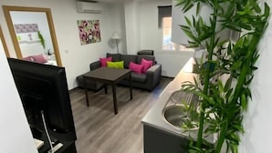 A compact living space with a kitchenette, a sofa with colorful cushions, a dining table, and a large mirror. - Reyna 2 Dormitorios (Málaga)