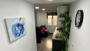 A hallway with a painting, a clock, a plant, and a kitchen area with a sink and countertop. - Reyna 2 Dormitorios (Málaga)