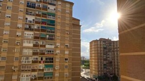 Korkea asuinkerrostalo, jossa on useita parvekkeita, parkkipaikka autoineen ja kirkas taivas.