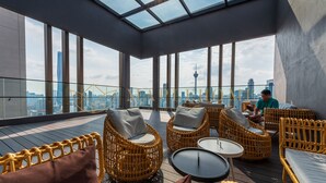 Eine Dachterrasse mit Korbmöbeln, einer Glaskuppel und Blick auf die Stadtlandschaft.