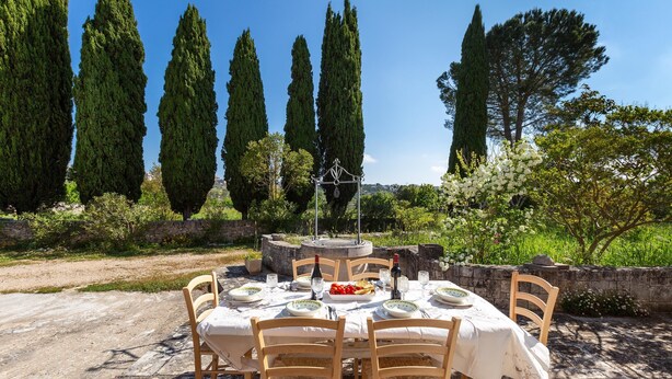 An outdoor dining area with a stone table and chairs, surrounded by tall cypress trees and a stone wall. - 3438 Villa Poggio dei Loti by Barbarhouse (Cisternino)